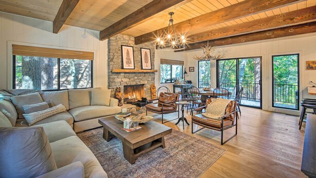A spacious living room with a stone fireplace, leather furniture, and large windows offering views of the outdoors. - Pet-Friendly Retreat w/ Game Room & Fire Pit! (Lake Arrowhead)
