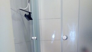 Une douche d’angle avec une porte en verre, des murs recouverts de carreaux blancs et une baignoire blanche.