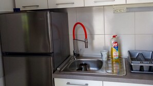 Une cuisine avec des meubles blancs, un réfrigérateur en acier inoxydable, un évier avec un robinet rouge et une bouteille de liquide vaisselle posée sur le plan de travail.