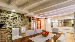 A dining area with a stone wall, wooden table, white chairs, and a fruit bowl. - Charming Pollensa Villa | Beautiful Views Of the Tramuntana Mountains | La. (Pollensa)