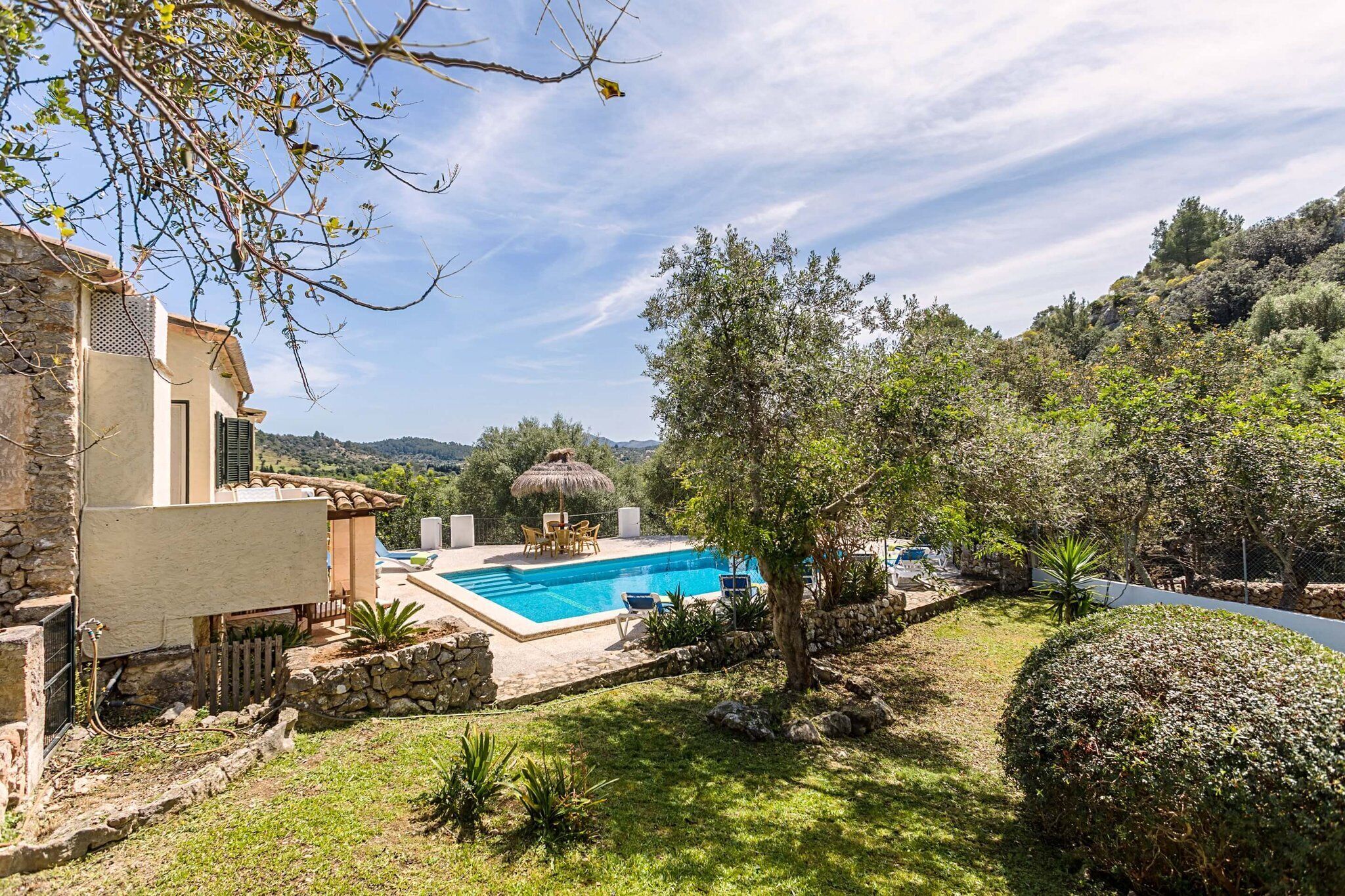 A villa with a swimming pool, stone walls, and a view of the hills.