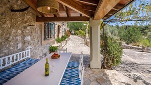A stone building with a wooden pergola, a table with a bottle and glass, and a view of a stone pathway leading to a garden. - Charming Pollensa Villa | Beautiful Views Of the Tramuntana Mountains | La. (Pollensa)