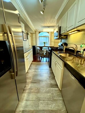 A kitchen with a stainless steel refrigerator, white cabinets, a granite countertop, and a window with a view.