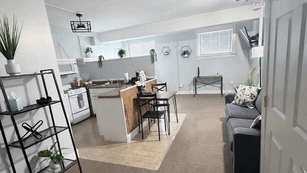 A modern kitchen with white appliances, a dining area with a wooden table and chairs, and a gray sofa in a spacious living room.