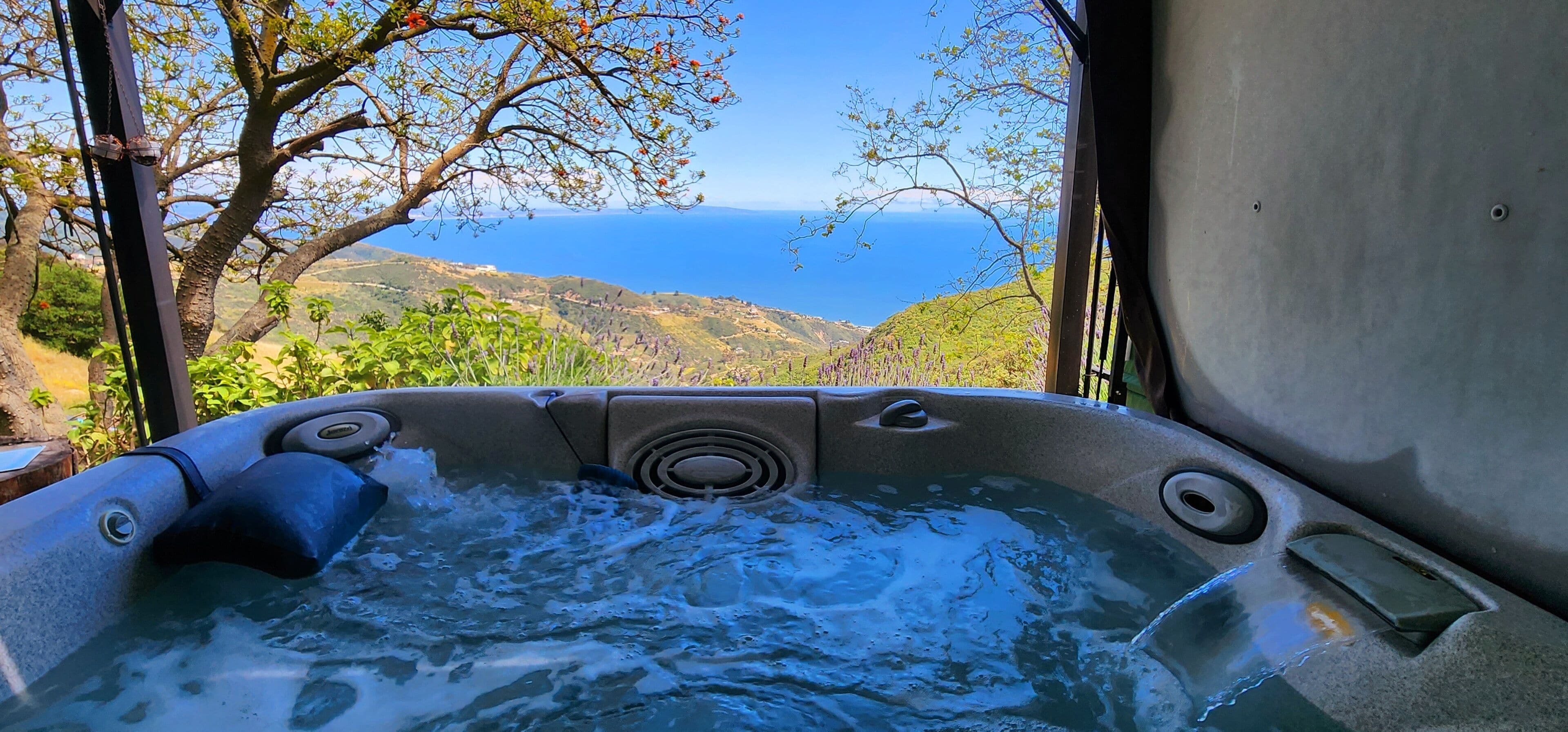 A hot tub with a view of the ocean and hills.