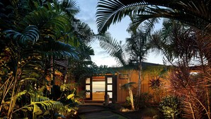 Un jardin tropical qui mène à une maison en bois dotée d’une porte en verre.