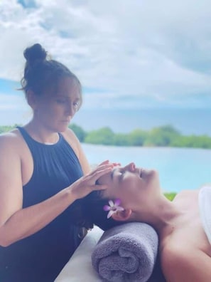 A person receiving a facial treatment outdoors with a lake view in the background.