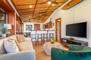 A living room with a sofa, a coffee table, and a TV. There is a kitchen area with a bar and stools. - Holualoa Sanctuary Hot Tub, Ocean Views, A/C 12 Min to Beach (Honalo)