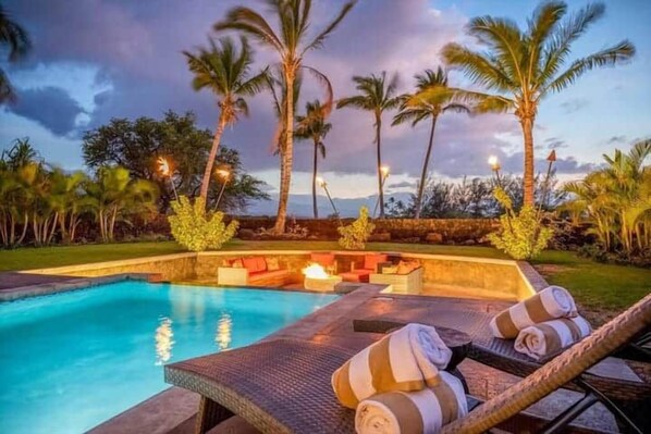 A swimming pool with lounge chairs and a fire pit area.