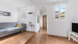 A modern living room with a grey sofa, a small table with a plant, a TV stand, and a window with a view of a building. - Home2Book Charming Attic Arucas Center, Terrace (Arucas)