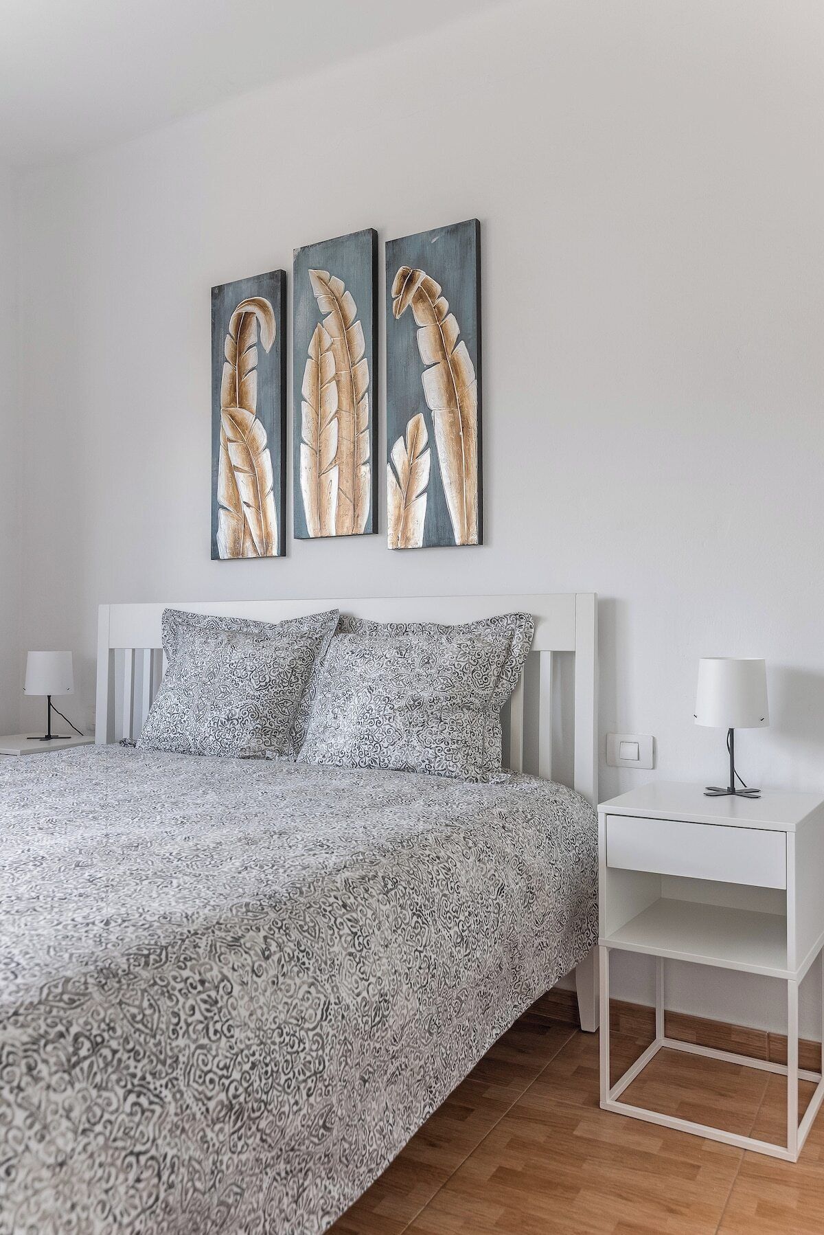A bedroom with a bed, two bedside tables, and three wall-mounted paintings.