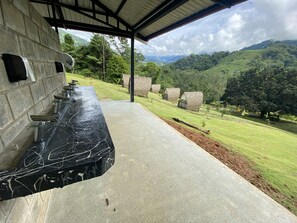 A covered outdoor area with a long counter, a stone wall, and a view of lush green hills and trees. - Esquipulas Rainforest (San Lorenzo)
