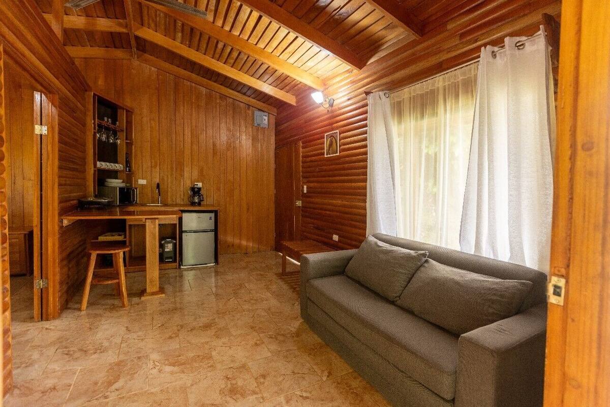 A cozy log cabin interior with a wooden dining table, a sofa, and a small kitchenette.