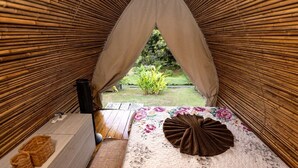 A room with a bamboo archway, a wooden table, a floral bedspread, and a small basket.