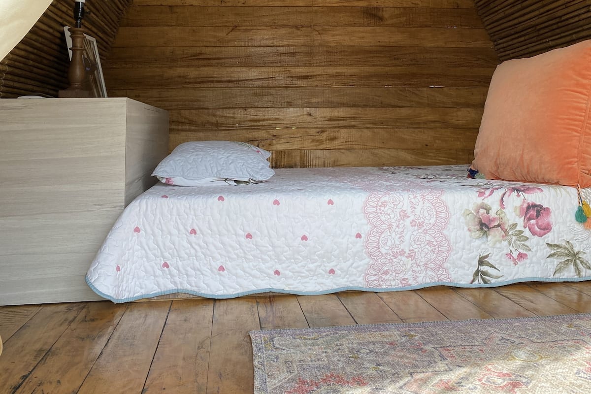 A cozy attic bedroom with a wooden ceiling, a bed with floral bedding, and a nightstand.