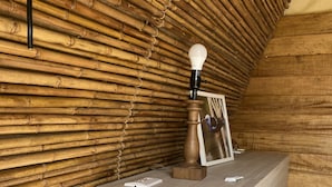 A room with a bamboo wall, a bedside table with a lamp, a framed photo, and a bed with a white comforter.