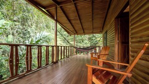 A wooden porch with a hammock and chairs, surrounded by lush greenery.
