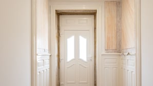 A hallway with a wooden floor, white walls, and a white door with glass panels. - Casa do Desassossego  (Monção)
