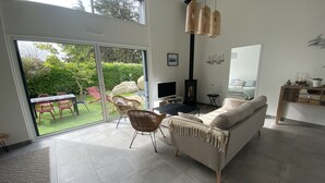 En moderne stue med sofa, TV og pejs. Der er et spiseområde med stole og bord, samt en stor skydedør, der fører ud til en have.