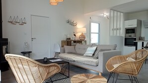 En moderne stue med en sofa, to fletstole, et sofabord og et spiseområde med bord og stole.