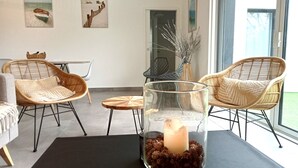 Et værelse med fletstole, et glastilbords med et stearinlys og kunst på væggene.