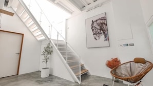 A modern interior with a staircase, a framed artwork, a potted plant, and a wicker chair. - Ling Inn (Kaohsiung)