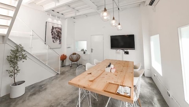 A modern office space with a wooden table, white chairs, a mounted TV, and a staircase with a plant. - Ling Inn (Kaohsiung)