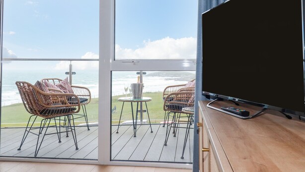 En balkon med fletstole og et lille bord, med udsigt over havet.