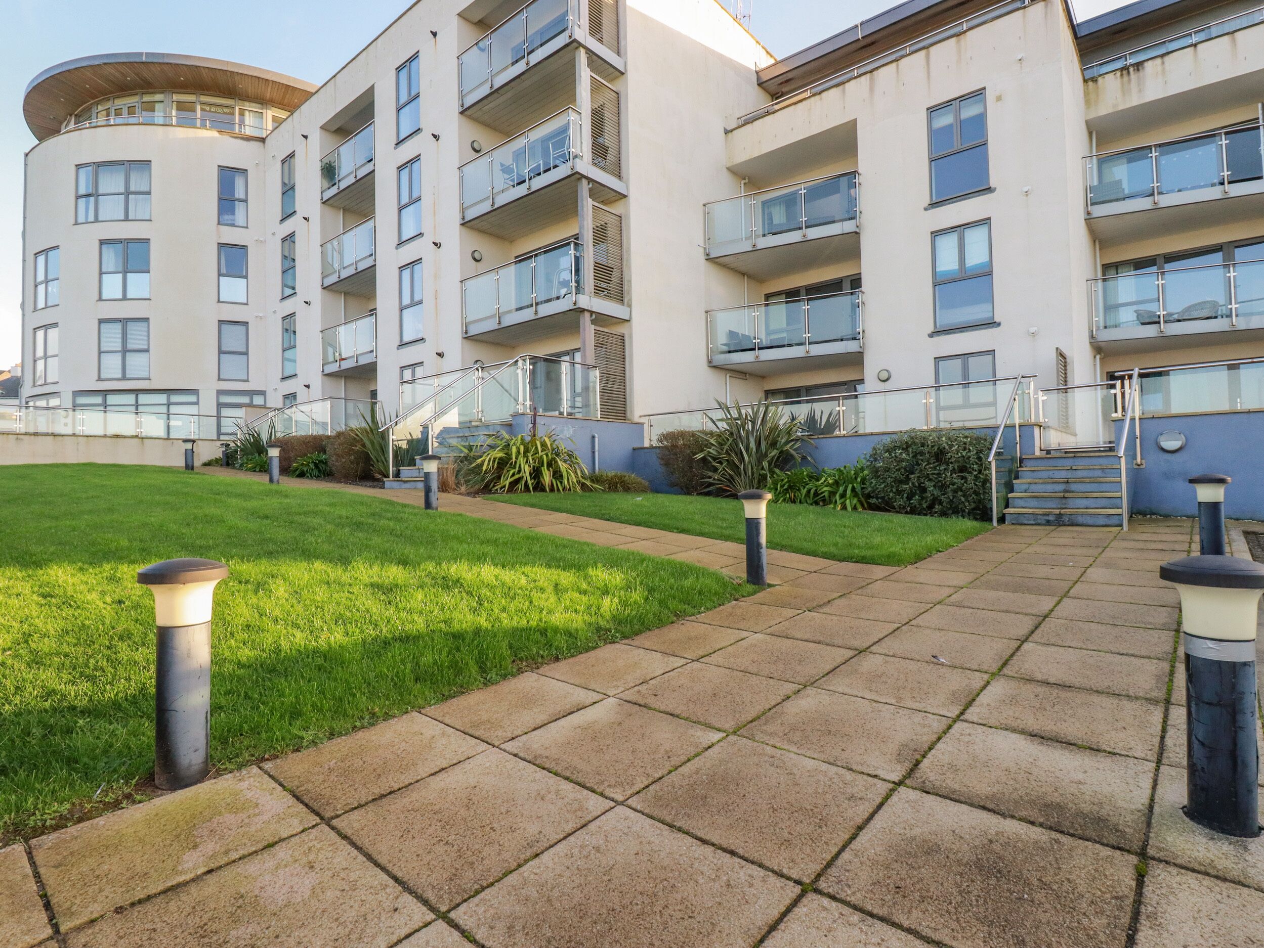 A modern apartment building with multiple balconies, a well-maintained lawn, and a clear sky.