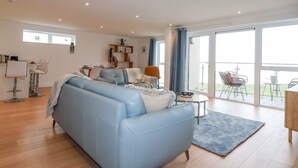 En rummelig opholdsstue med blå sofa, spisebord og balkon med udendørs møbler.