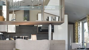 Un salon moderne avec un canapé, une étagère en verre où sont posés des verres à vin, et un coin cuisine en arrière-plan.