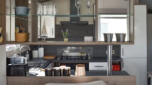 Une cuisine compacte équipée d’une cuisinière intégrée, d’un évier et d’un four à micro-ondes. Des étagères en verre, situées au-dessus de la cuisinière, servent à ranger divers objets.
