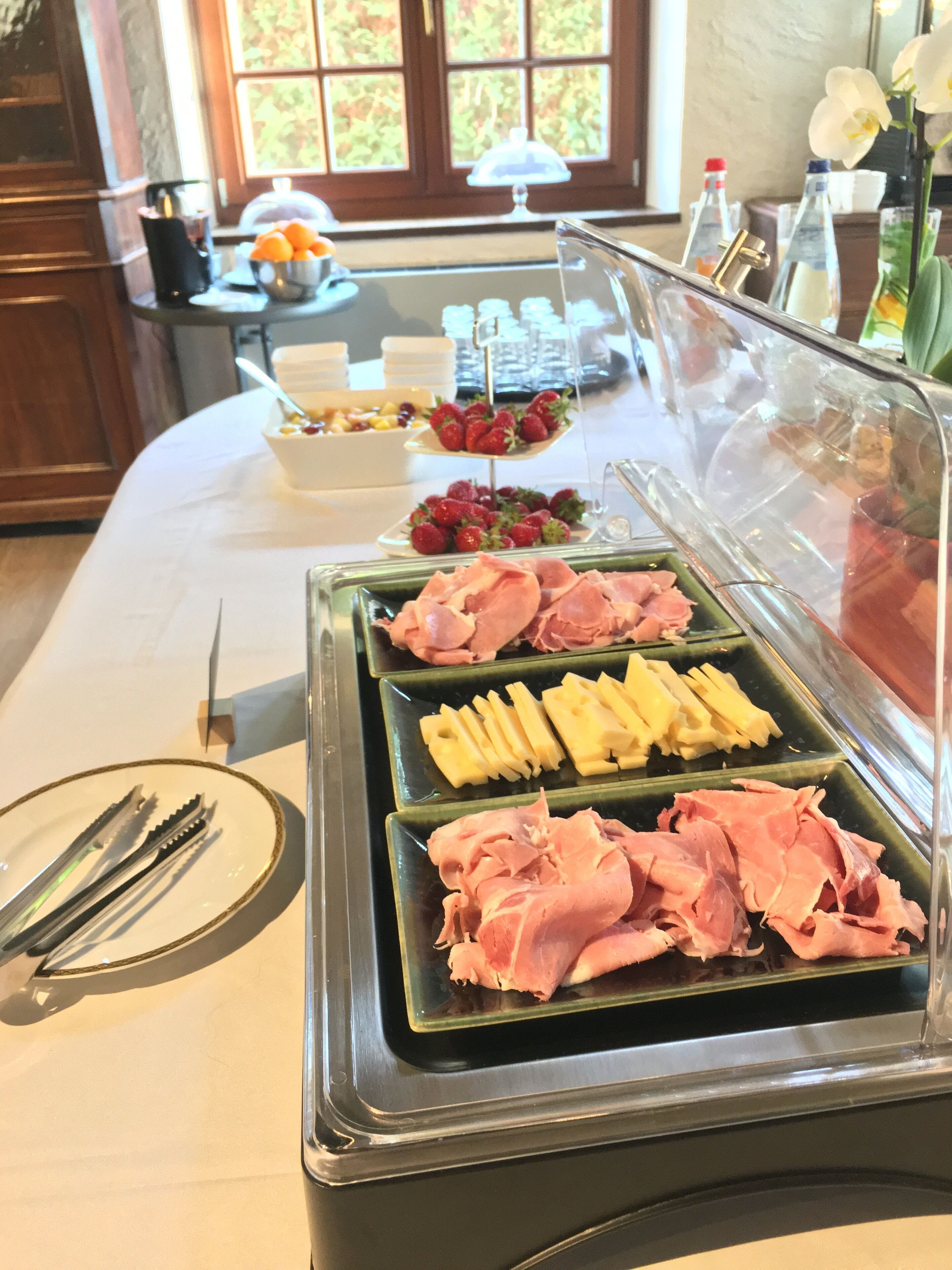 A buffet setup with various food items including ham, cheese, and strawberries.