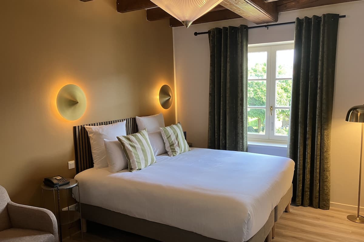 A large bed with white linens, a bedside table with a phone, and a lamp.