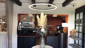 A reception area with a counter, a display case, a vase with flowers, a television, and a sign indicating the bakery section. - Relais Manderen (Manderen-Ritzing)
