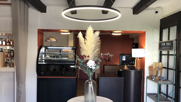 Un área de recepción con mostrador, vitrina, un jarrón con flores, televisor y un cartel que indica la panadería.