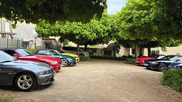 Un estacionamiento de grava con varios coches aparcados bajo árboles.