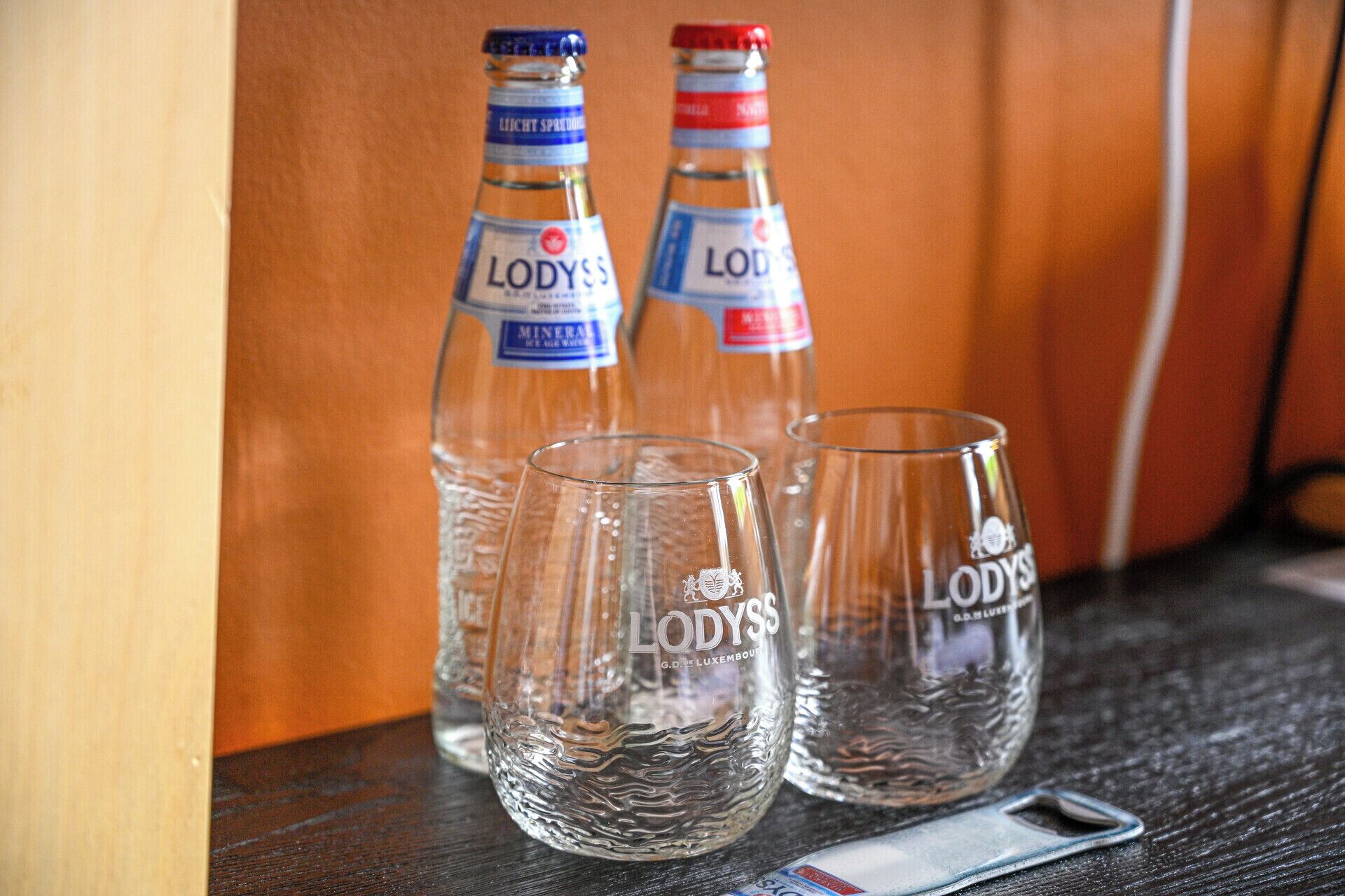 Two bottles of Lodyss mineral water and two clear glasses on a wooden surface.