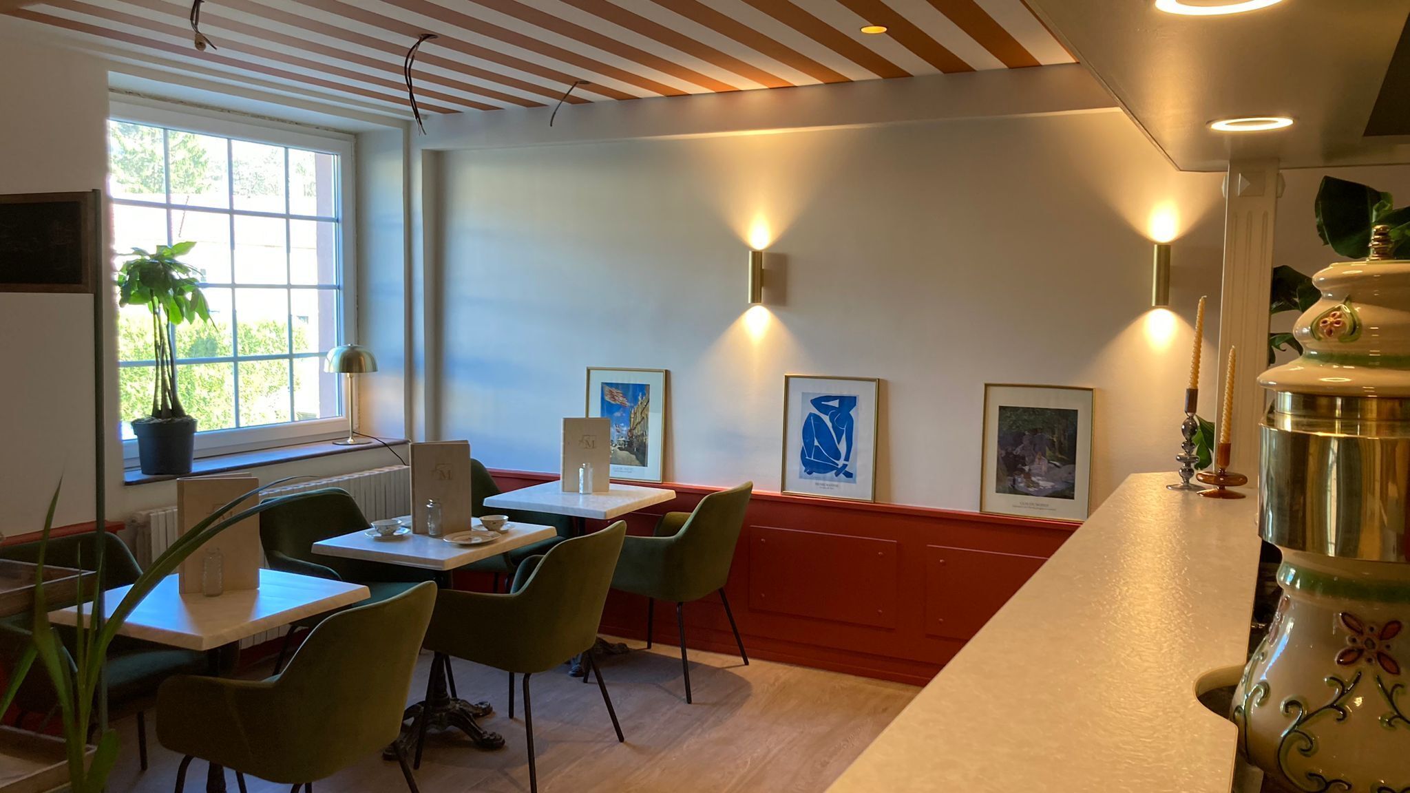 A restaurant with wooden ceiling beams, green chairs, and framed artwork on the walls.