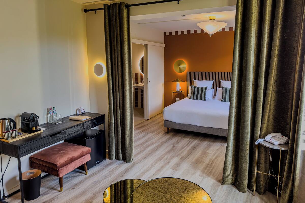 A hotel room with a bed, desk, and a bathroom visible through a curtain.