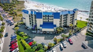 Ein mehrstöckiges Hotel mit blauem Dach, einem Parkplatz und Blick auf den Strand.