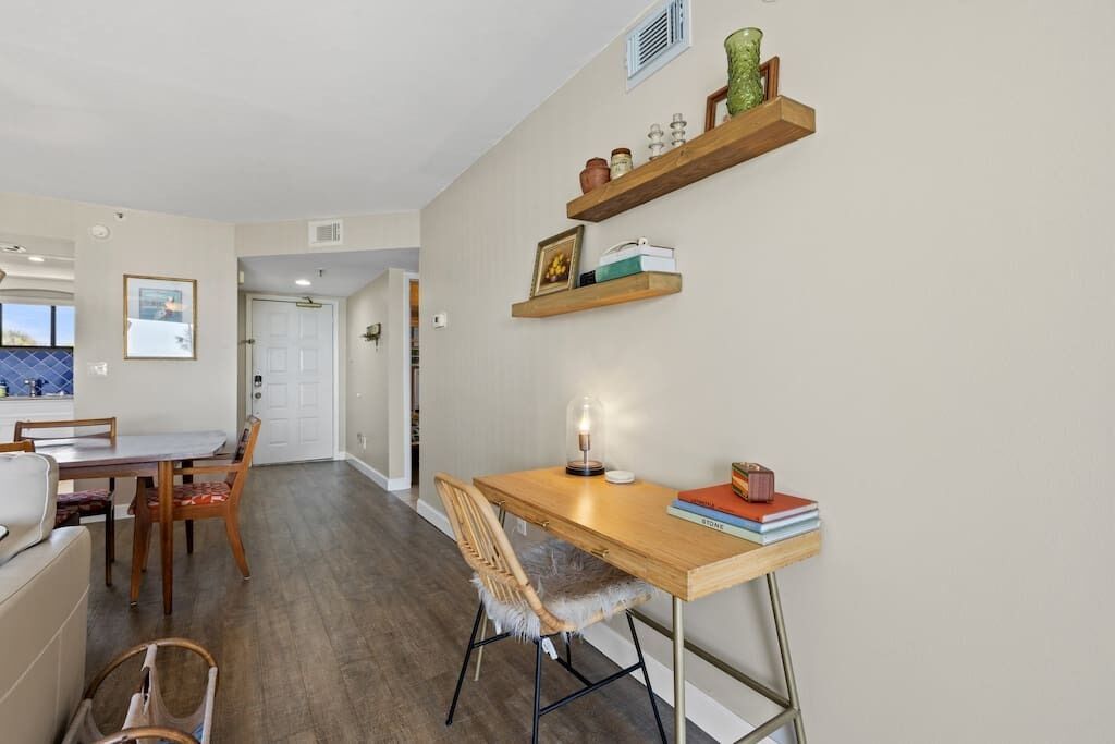 A dining area with a wooden table, chairs, and a hanging shelf with decorative items.
