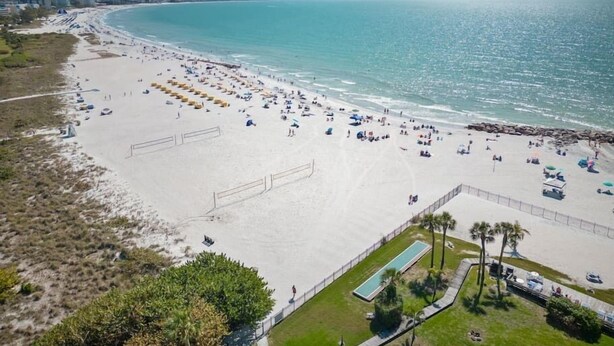 Ein Strand mit vielen Sonnenschirmen und Liegestühlen, einem umzäunten Schwimmbad und freiem Blick auf den Ozean.