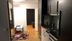 A narrow kitchen with a refrigerator, sink, and cabinets. A small rug and a chair are visible in the background. - Apartment in Årsta Stockholm 244 (Arsta)