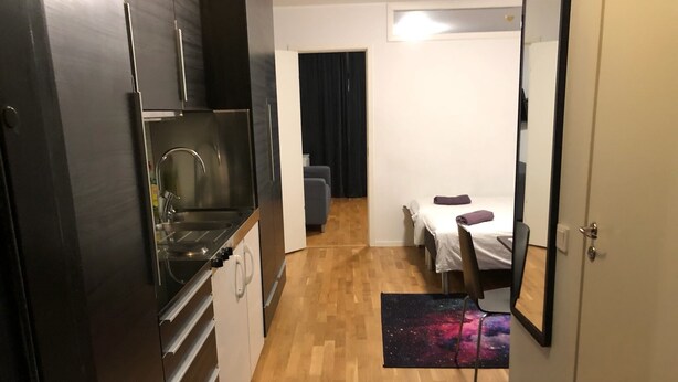 A compact kitchen with modern appliances, a small dining area with a table and chairs, and a bedroom with a bed and a nightstand. - Apartment in Årsta Stockholm 244 (Arsta)