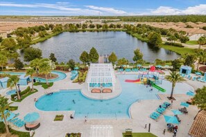 A large outdoor swimming pool with a water slide, surrounded by lounge chairs and umbrellas.