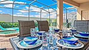 Ein mit Glaswänden umgebenes Esszimmer mit Blick auf einen Pool, Sitzgelegenheiten im Freien und einem klaren Himmel.