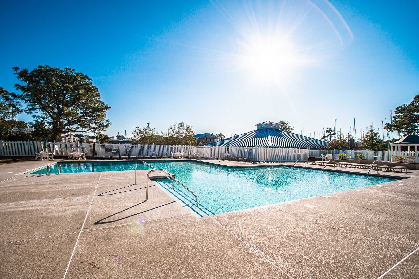 A rectangular swimming pool with a metal ladder, surrounded by a white fence and lounge chairs.