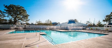 A rectangular swimming pool with a metal ladder, surrounded by a white fence and lounge chairs.