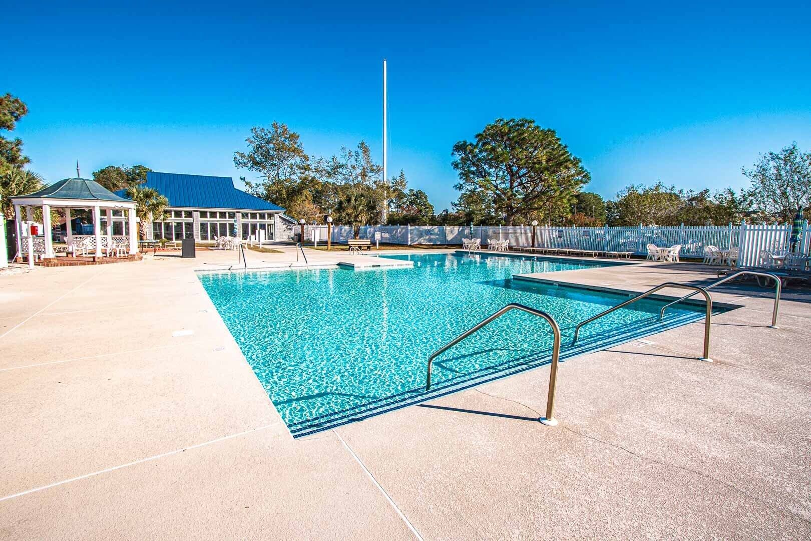 A clear blue swimming pool with a lifeguard stand, lounge chairs, and a covered pavilion.